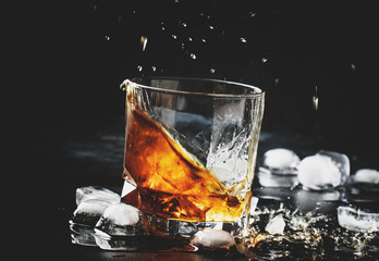 Whiskey with ice, splashes out of glass, dark background, toned image, selective focus