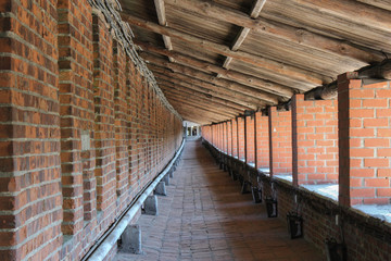 monastic wall of red brick with columns and wooden roof