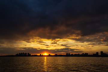 sunset over the river in the city and the reflection of the sun in the water. Storm clouds in the sky