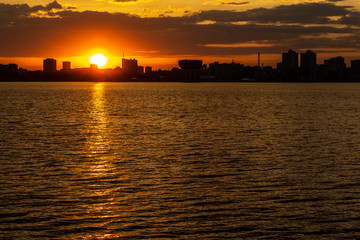 sunset over the river in the city with silhouettes of buildings and the reflection of the sun in the water