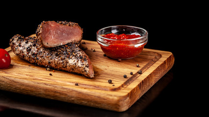 two juicy beef pepper steak with a air fryer medium rare, with a red sharp sauce on a wooden board, on a black background. Copy space