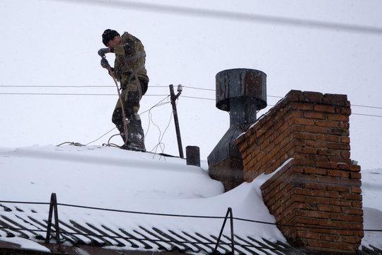 Chimney sweep man in work uniform cleaning chimney on building roof .