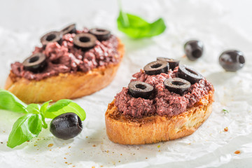 Tasty bruschetta with black olives on white table