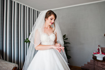 Fototapeta na wymiar Portrait of a beautiful bride in gorgeous white dress standing in the room and looking at her ring.