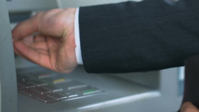 Man entering personal code on ATM and receiving dollar bills, counting money