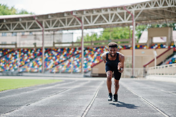 African american male athlete in sportswear racing alone down a running track at stadium.