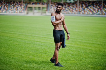 African american male athlete sexy sport bare torso man with running sports arm case for mobile phone, posed at green grass of football stadium.