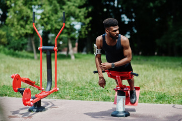 Fototapeta na wymiar African american male athlete sport man with running sports arm case for mobile phone, doing exercises on the street workout simulators.
