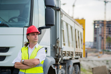 Truck driver in front of a truck on a construction site with his arms crossed