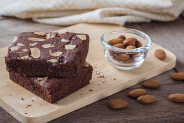 Chocolate brownie topping with almond slices on wooden plate.