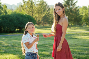 Fototapeta premium beautiful long-haired little girl (daughter) toothy smile long hair and mother eating pistachio ice cream in the park heat summer trip. youth and freshness concept