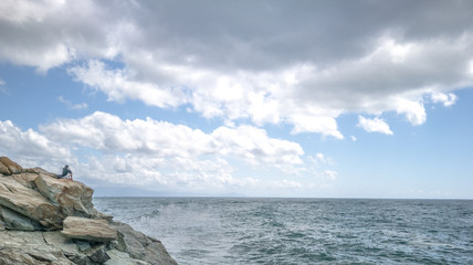 Fototapeta na wymiar Lonely girl on a rock cliff, observing the ocean