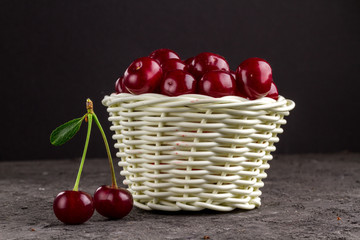 White basket with ripe cherries on a black background.