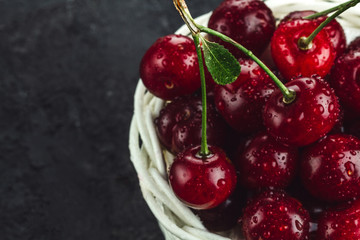 Red cherries in a wicker basket on a black background. Copy space