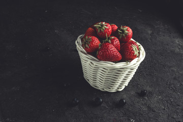 Fresh strawberries in a white basket on a black background.