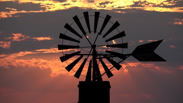 Traditional rustic old windmill spinning silhouette and sunset red clouds sky