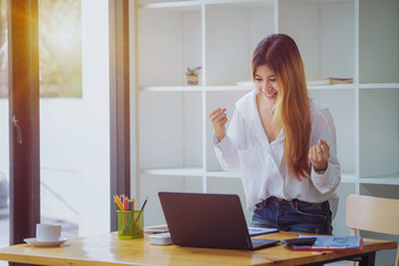 Beautiful Asian girl celebrate with laptop in office.	