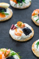 Selection of cocktail blinis with salmon, cured bresaola, crayfish, caviar, quail eggs and sour cream - gourmet party food