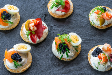 Selection of cocktail blinis with salmon, cured bresaola, crayfish, caviar, quail eggs and sour cream - gourmet party food - top view