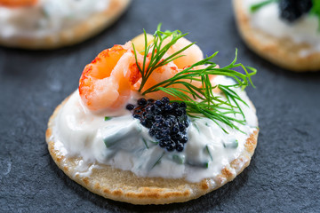 Cocktail blinis with crayfish, caviar and sour cream - gourmet party food.