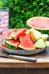 Slices of sweet, refreshing watermelon and honeydew melon on a garden table. Summer outdoor eating.
