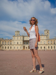 A smiling woman tourist with small orange backpack in the center of Gatchina. Tourism in Europe, woman tourist at the Palace. 