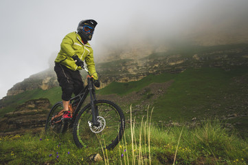An adult mtb cyclist on a mountain bike at the foot of a cliff surrounded by green grass. Low...