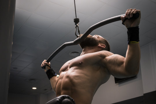 Hombre fuerte con grandes m&uacute;sculos entrenando jal&oacute;n al pecho en el gimnasio. Ponerse en forma.