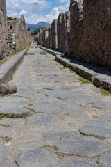  Empty stone street with ruins in Pompeii, Italy. Antique road in italian ancient town. Abandoned street in perspective. Pompeii landmark. History and architecture concept. 