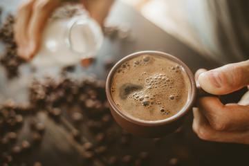 Man pouring milk in steamed coffee