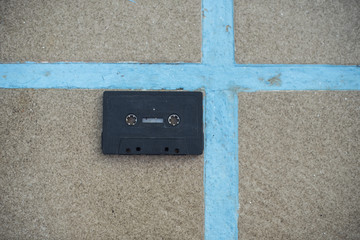 Bodegón minimalista de cinta de casete de color negro sobre una superficie de piedra con líneas azules en forma de cruz