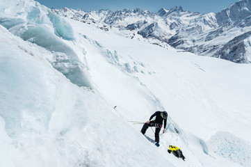 A professional mountaineer in a helmet and ski mask on the insurance does notch the ice ax in the glacier. The work of a professional climber in winter on a glacier against the blue sky