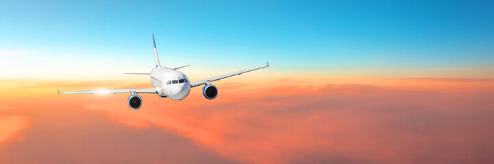 Passenger aircraft cloudscape with white airplane is flying in the orange sky with colorful sunset, panorama view.
