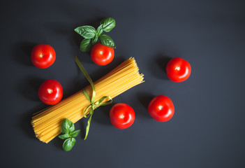 Naklejka na ściany i meble Raw spaghetti pasta with fresh tomatoes and basil leaves on dark background