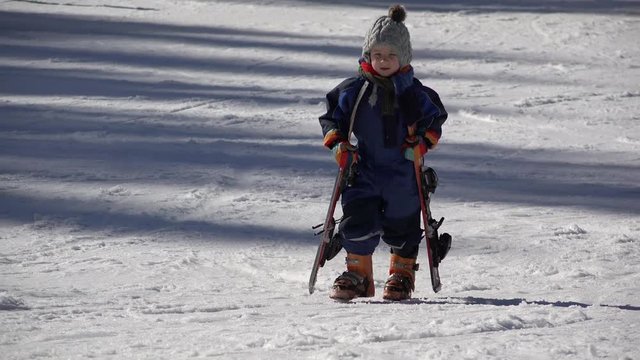 Little child carry heavy ski equipment, loving winter sport