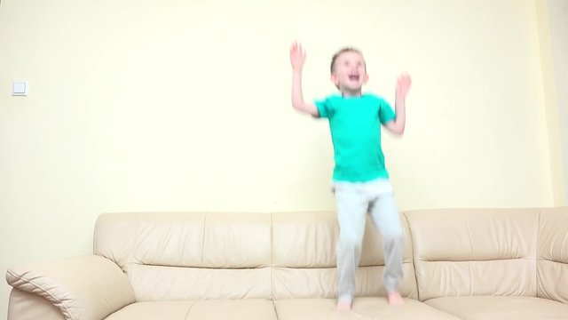 Happy child jumping on sofa, rise up hands, enthusiastic dance, free childhood, kid tired falling down