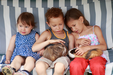 three children are sitting in a hammock and playing her guinea pig pet animal.