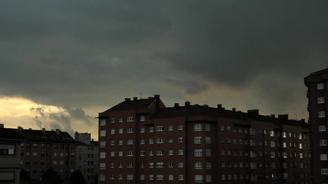 Deep evening sunset above the multistorey red brick residential buildings with dramatic clouds moving fast at the night sky, time-laps, with orange colors of moving doen sun