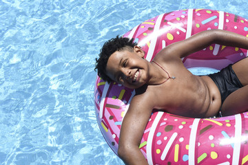 Happy cute little african-american boy lying on an inflatable donut circle  in the swimming pool in...