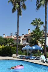 Happy cute little african-american boy lying on an inflatable donut circle  in the swimming pool in the hotel. Cool summer holidays for children and kids. Active games on the water.  Pink donat. 