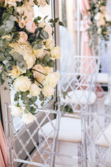 Flower arrangement of white roses and eucalyptus next to transparent chairs adorns the wedding ceremony zone in classical style