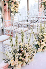 Rows of transparent chairs decorated with flower compositions of roses and white buttercups in the wedding ceremony area