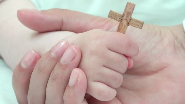 Detail of mother hand holding baby hand with christian cross, early education, real values to guide a new life