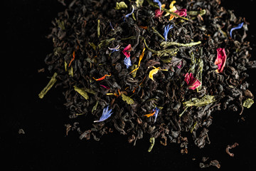 A mixture of dry leaves of black and green tea with flowers on a dark background