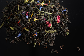 A mixture of dry leaves of black and green tea with flowers on a dark background
