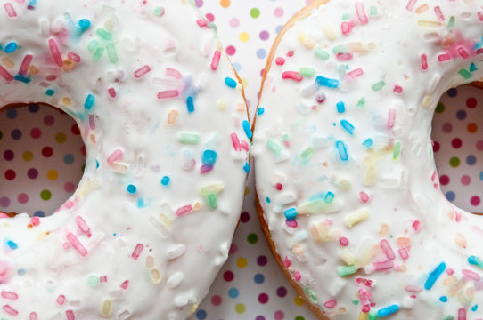 two glazed donuts decorated with colorful sprinkles