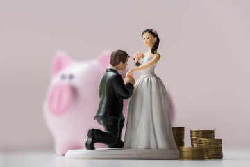 statuette of groom and bride with coins on pink background. Moneybox and wedding economy