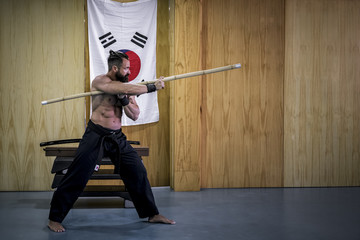 Hombre fuerte con grandes músculos entrenando artes marciales con arma han bo. Defensa personal...