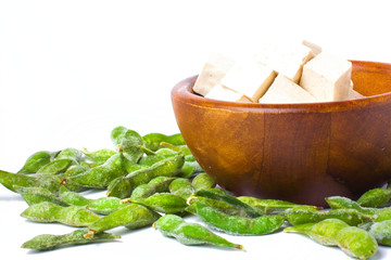 Tofu in wooden bowl with green edamame on white background