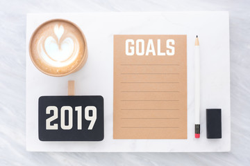 2019 goals on brown recycle paper with pencil,clip blackboard,pencil,eraser and coffee cup on white and grey marble table.mock up for adding text,new year resolution concept.